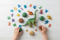 Flat lay of dinosaur sensory kit contents with resin alphabet letters, dinosaur figurines, toy and playdough with children's hands playing