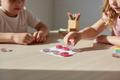 Two children playing resin glitter Tic Tac Toe game with sparkly pink flower and heart pieces on a wooden table